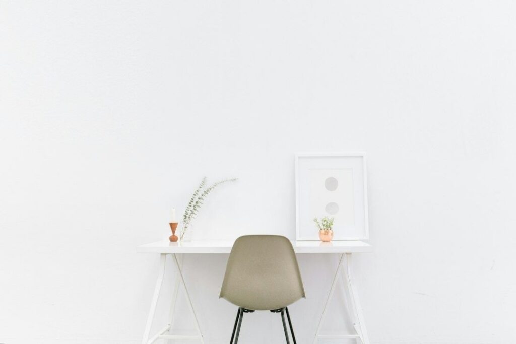 Minimalist white desk with a muted chair, plants, and framed art