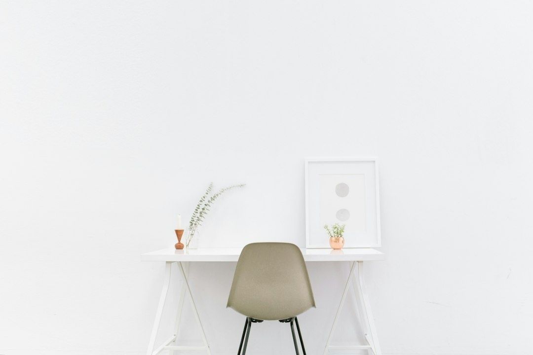 Minimalist white desk with a muted chair, plants, and framed art