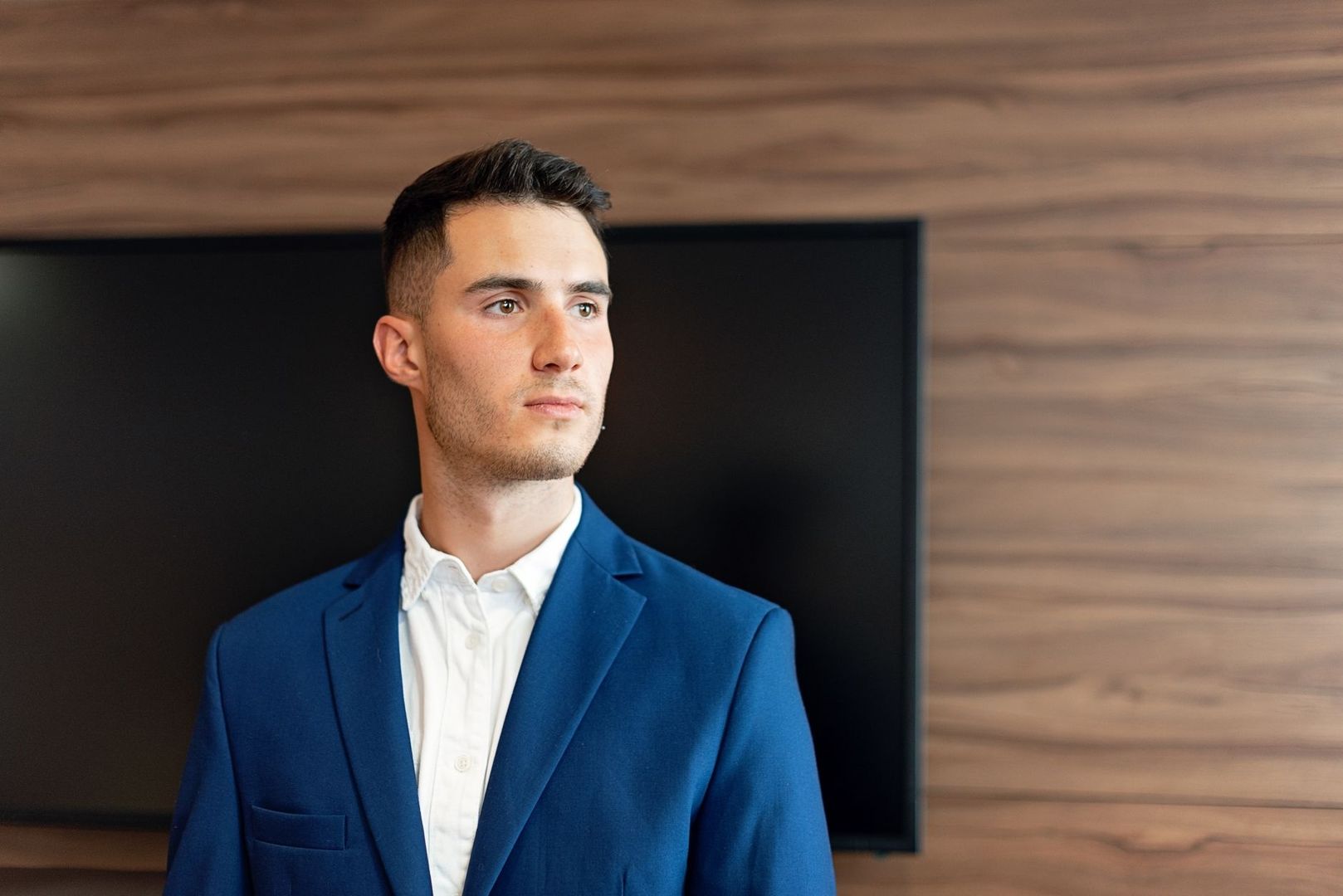 Man in a vivid blue blazer and white shirt against a wood wall
